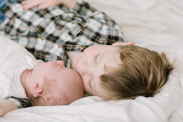 Großer Bruder und neugeborene kleine Schwester kuscheln im Bett - CAVF81569