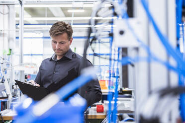 Mann mit Klemmbrett macht sich Notizen in einer Fabrik - DIGF10941