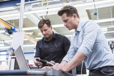 Zwei Männer benutzen einen Laptop in einer Fabrik - DIGF10944