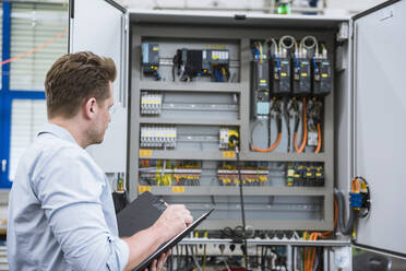 Techniker mit Klemmbrett bei der Arbeit an einer Schaltung in einer Fabrik - DIGF10958