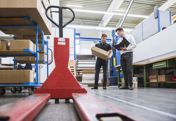 Two men with parcel and clipboard in storehouse of a factory - DIGF10959