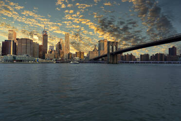 USA, New York, New York City, East River and Brooklyn Bridge at dramatic sunrise with Manhattan skyline in background - LOMF01134