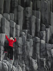 Frau klettert auf Basaltsäulen in Südisland - CAVF81907