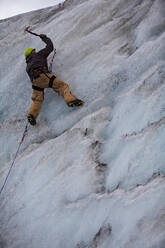 Young man climbing ice wall at Solheimajokull glacier in Iceland - CAVF81948