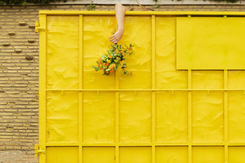Arm einer Frau hängt an einem gelben Behälter und hält einen Blumenstrauß, lizenzfreies Stockfoto