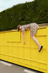 Exhausted woman hanging over edge of yellow container - ERRF03844