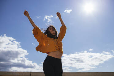 Unbeschwerte Frau tanzt auf Dachterrasse im Sonnenlicht - GMLF00217