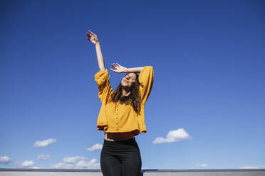 Carefree woman dancing on roof terrace in sunlight - GMLF00218