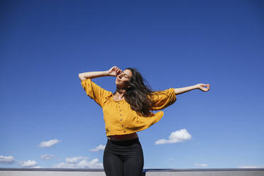 Carefree woman dancing on roof terrace in sunlight - GMLF00219