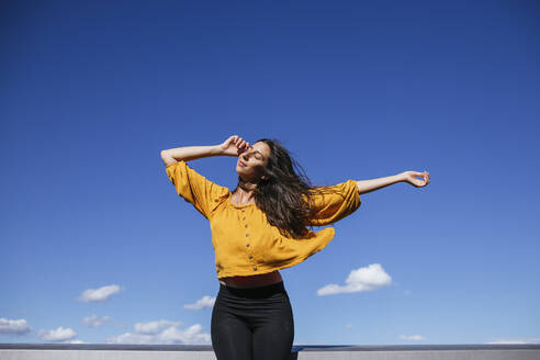 Carefree woman dancing on roof terrace in sunlight - GMLF00219