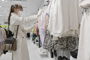 Woman with face mask and disposable gloves shopping in a fashion store - AHSF02589