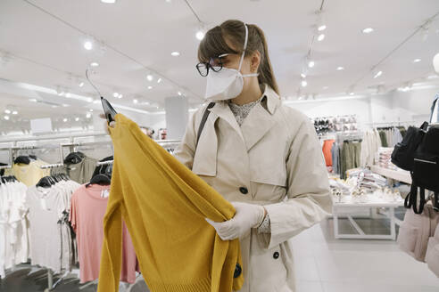 Frau mit Gesichtsmaske und Einweghandschuhen beim Einkaufen in einem Modegeschäft - AHSF02591