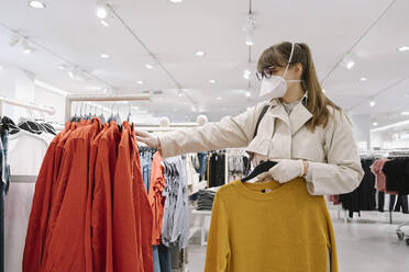 Woman with face mask and disposable gloves shopping in a fashion store - AHSF02592