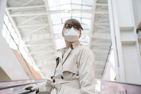 Woman with face mask and disposable gloves on an escalator in a shopping center stock photo