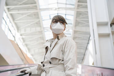 Woman with face mask and disposable gloves on an escalator in a shopping center - AHSF02594