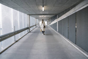 Rear view of woman walking in corridor of a car park after shopping - AHSF02606