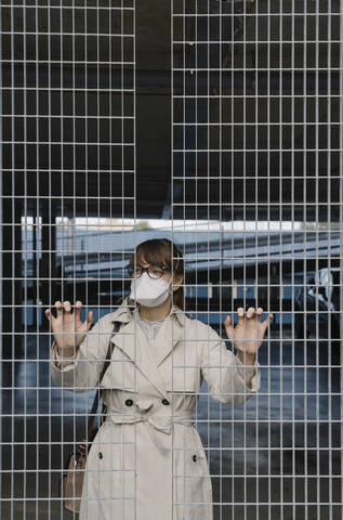 Woman wearing face mask standing behind grating in a car park stock photo