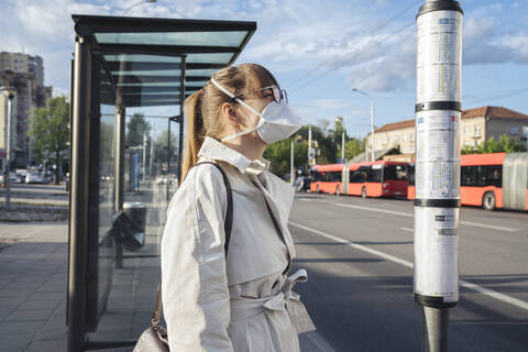 Frau mit Gesichtsmaske bei der Überprüfung des Fahrplans der öffentlichen Verkehrsmittel in der Stadt, lizenzfreies Stockfoto