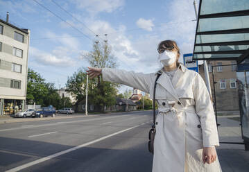 Woman wearing face mask in the city hailing a taxi - AHSF02615