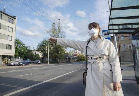 Frau mit Gesichtsmaske in der Stadt, die ein Taxi ruft - AHSF02615