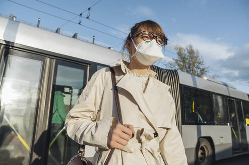 Woman wearing face mask getting off the bus in the city - AHSF02618