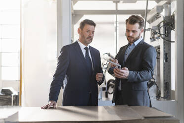 Two businessmen having a meeting in a factory examining workpiece - DIGF10997