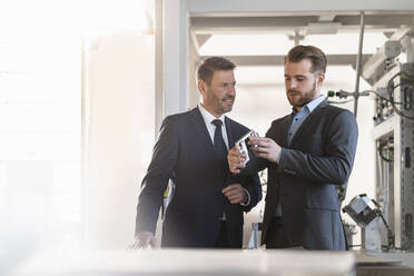 Two businessmen having a meeting in a factory examining workpiece - DIGF10998