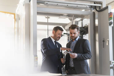 Two businessmen having a meeting in a factory examining workpiece - DIGF11000