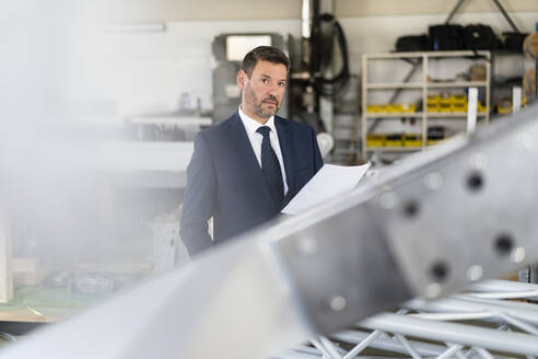 Porträt eines reifen Geschäftsmannes mit Papier in einer Fabrik - DIGF11005