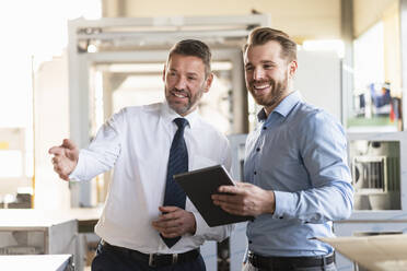 Two smiling businessmen with tablet having a meeting in a factory - DIGF11009