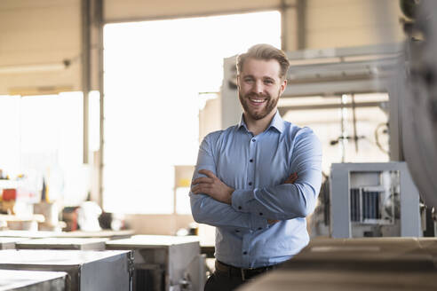 Porträt eines glücklichen jungen Geschäftsmannes in einer Fabrik - DIGF11011