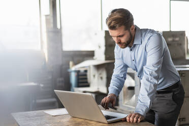 Young businessman using laptop in a factory - DIGF11026