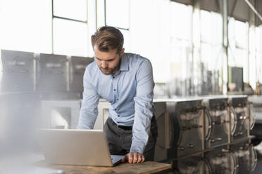 Young businessman using laptop in a factory - DIGF11027