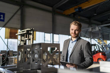 Porträt eines lächelnden jungen Geschäftsmannes mit Tablet in einer Fabrik - DIGF11042