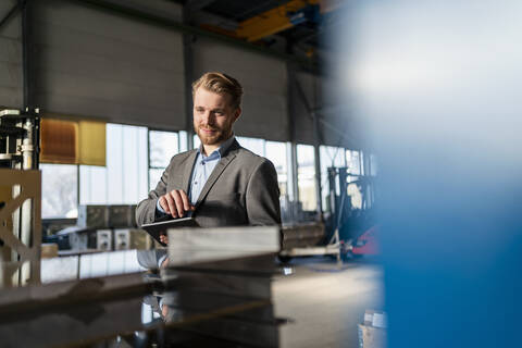 Porträt eines lächelnden jungen Geschäftsmannes mit Tablet in einer Fabrik, lizenzfreies Stockfoto