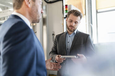 Two businessmen having a meeting in a factory discussing workpiece - DIGF11047