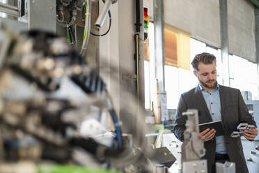 Junger Geschäftsmann mit Tablet und Werkstück in einer Fabrik - DIGF11054