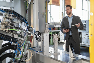 Young businessman with tablet and workpiece at a machine in a factory - DIGF11056