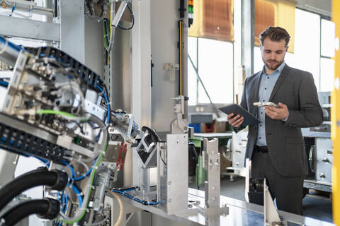 Junger Geschäftsmann mit Tablet und Werkstück in einer Fabrik, lizenzfreies Stockfoto