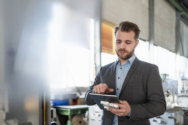 Junger Geschäftsmann mit Tablet und Werkstück in einer Fabrik - DIGF11058