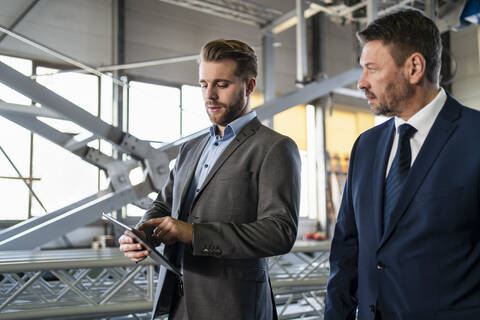 Zwei Geschäftsleute mit Tablet haben eine Sitzung in einer Fabrik, lizenzfreies Stockfoto