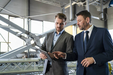 Zwei Geschäftsleute mit Tablet haben eine Sitzung in einer Fabrik, lizenzfreies Stockfoto