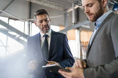 Zwei Geschäftsleute mit Tablet haben eine Sitzung in einer Fabrik, lizenzfreies Stockfoto