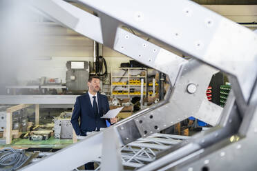 Älterer Geschäftsmann hält Papier in einer Fabrik - DIGF11082