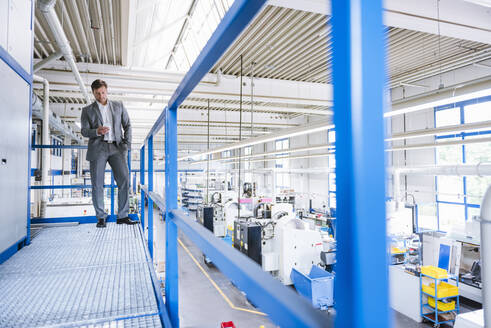 Geschäftsmann mit Smartphone im oberen Stockwerk einer Fabrik - DIGF11116