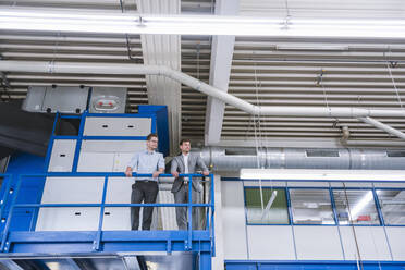 Zwei Geschäftsleute stehen im oberen Stockwerk einer Fabrik - DIGF11118