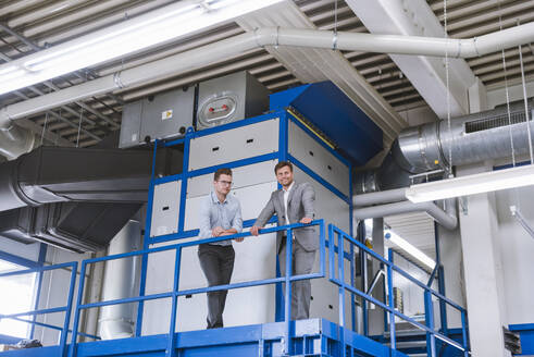 Zwei Geschäftsleute stehen im oberen Stockwerk einer Fabrik - DIGF11119
