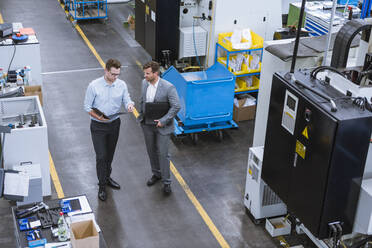 Zwei Geschäftsleute mit Klemmbrett im Gespräch in einer Fabrik - DIGF11120