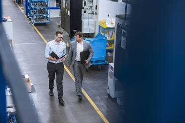 Two businessmen with clipboard walking and talking in factory - DIGF11122