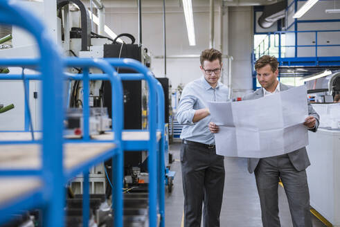 Zwei Geschäftsleute besprechen einen Plan in einer Fabrik - DIGF11131